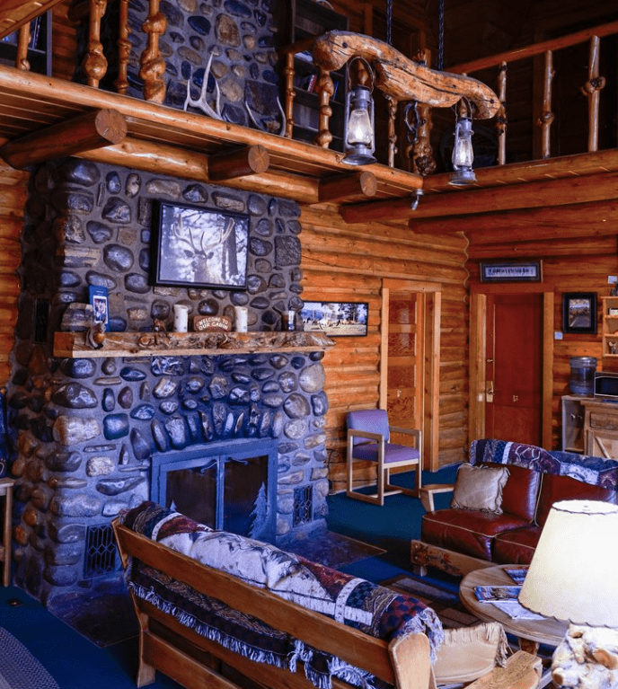 Stone fireplace inside of lobby of lodge with walls made of logs. 