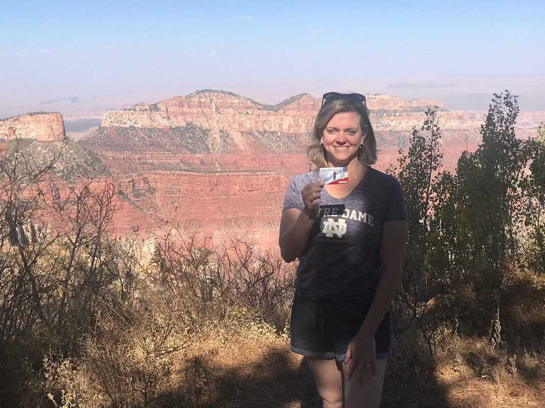 Lyn holding National Parks Pass in front of Grand Canyon