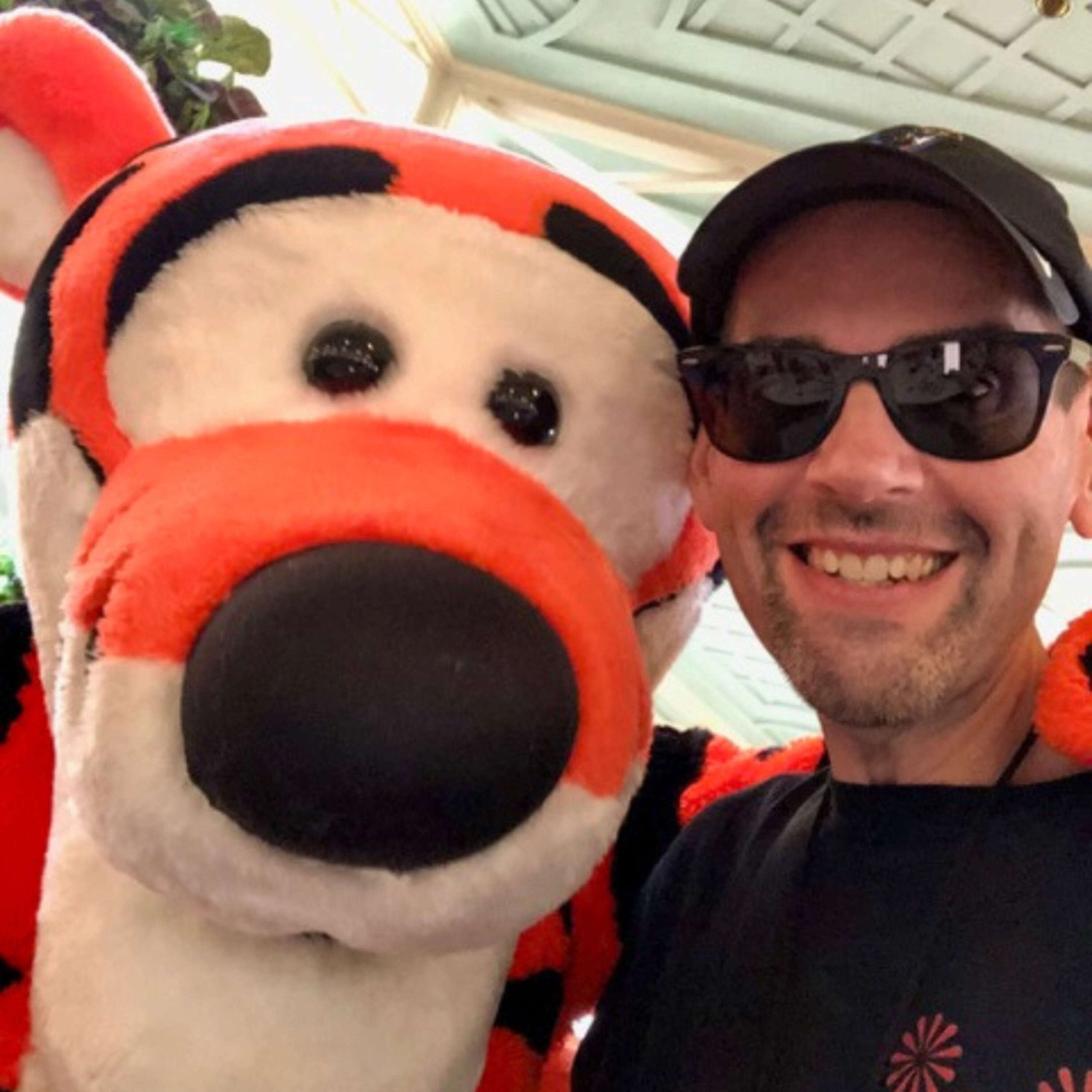 A man in sunglasses is posing with a tiger mascot.
