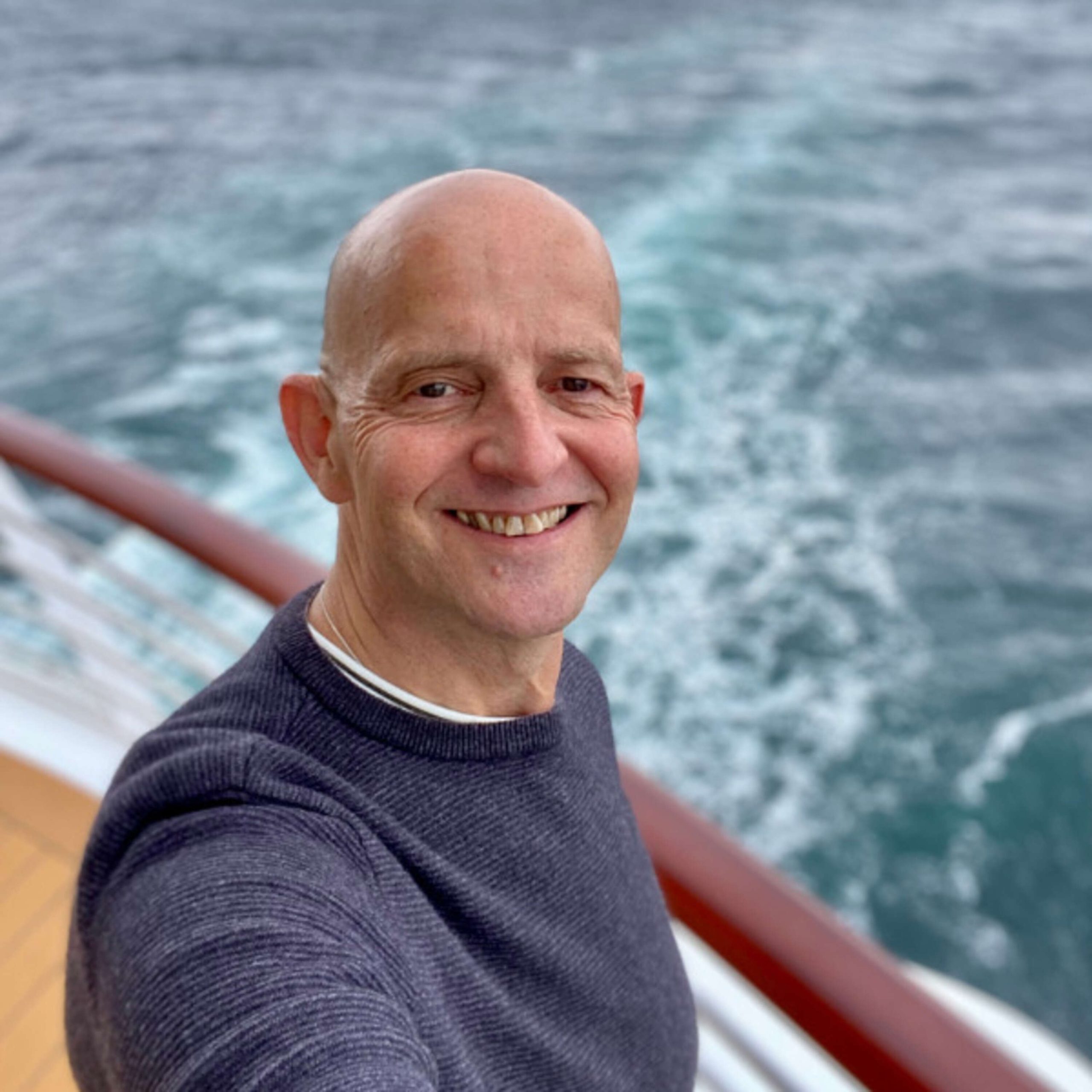 A bald man taking a selfie on the deck of a cruise ship.