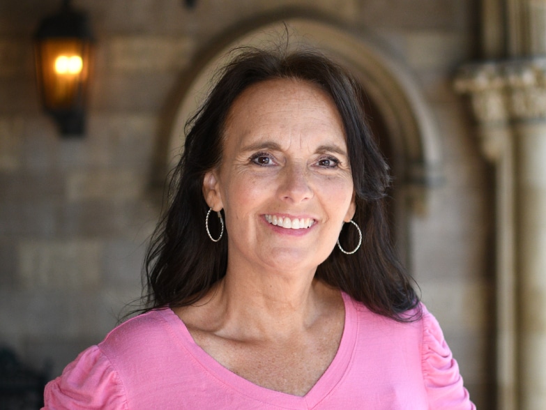 A woman in a pink shirt smiling in front of an archway.