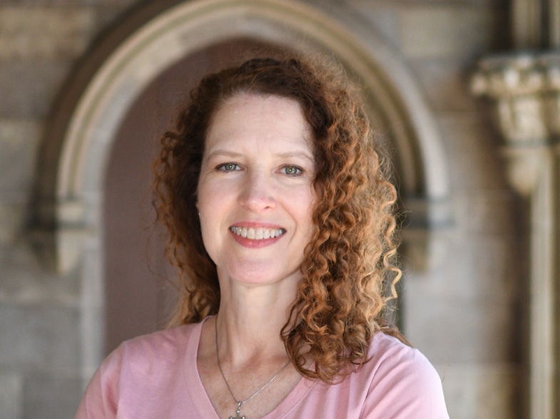 A woman with curly hair smiling in front of an archway.