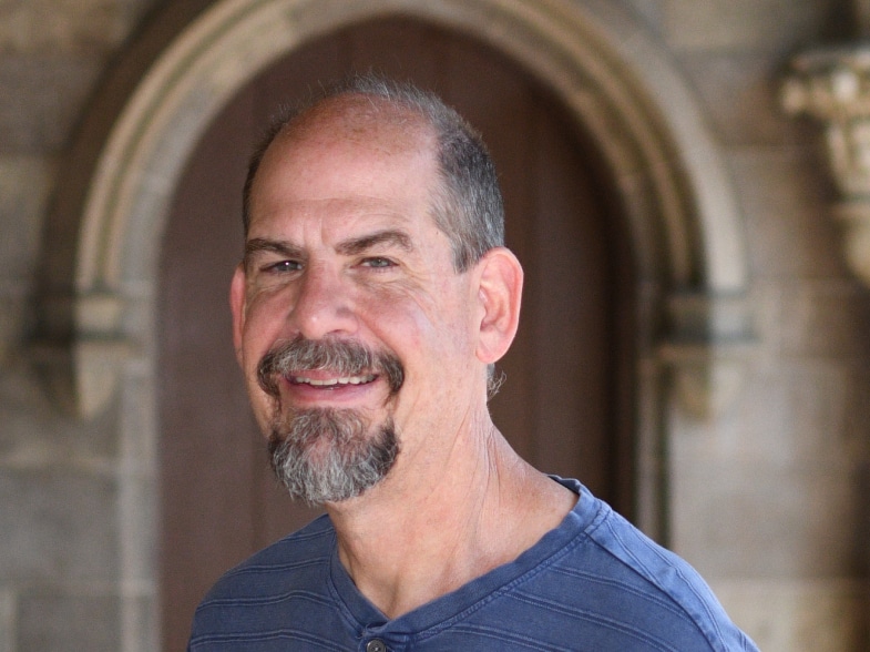 A man with a beard smiling in front of an archway.