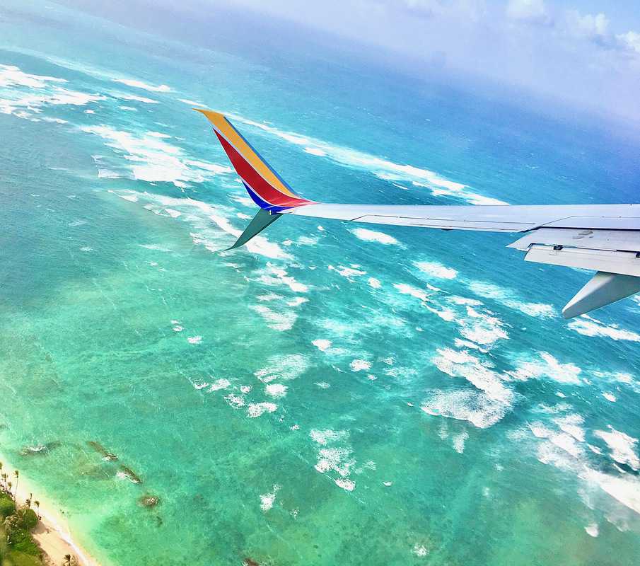 A Southwest airplane wing flying over a beach and ocean in Hawaii.